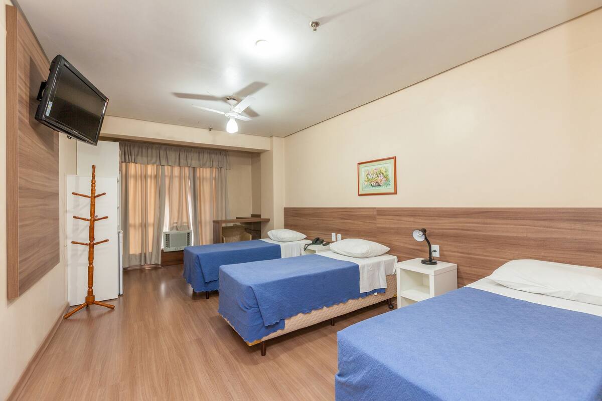 Habitación de hotel con tres camas, televisión, ventilador de techo y escritorio con silla.