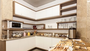 A kitchen with a microwave, buffet setup, and various food items. - Letto Hotel Porto Alegre (Porto Alegre)
