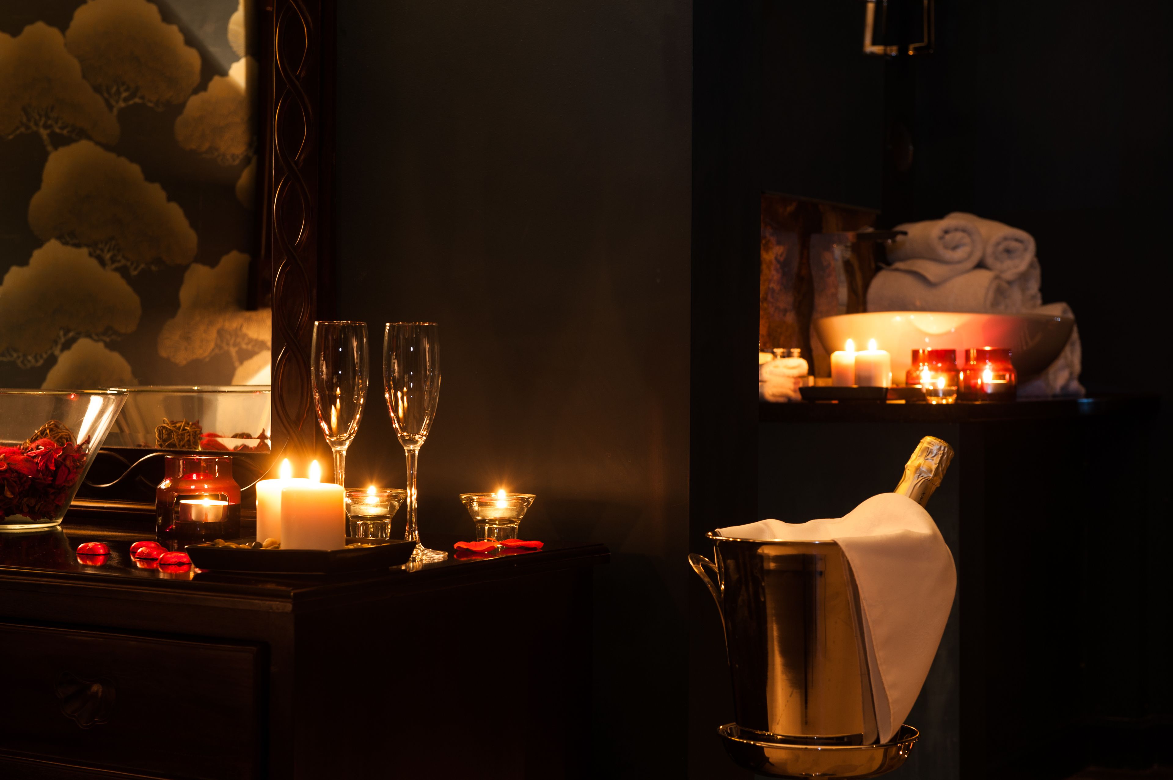 Um quarto com pouca luz, com uma mesa posta para dois, incluindo um balde de champanhe, velas e uma cesta de frutas.