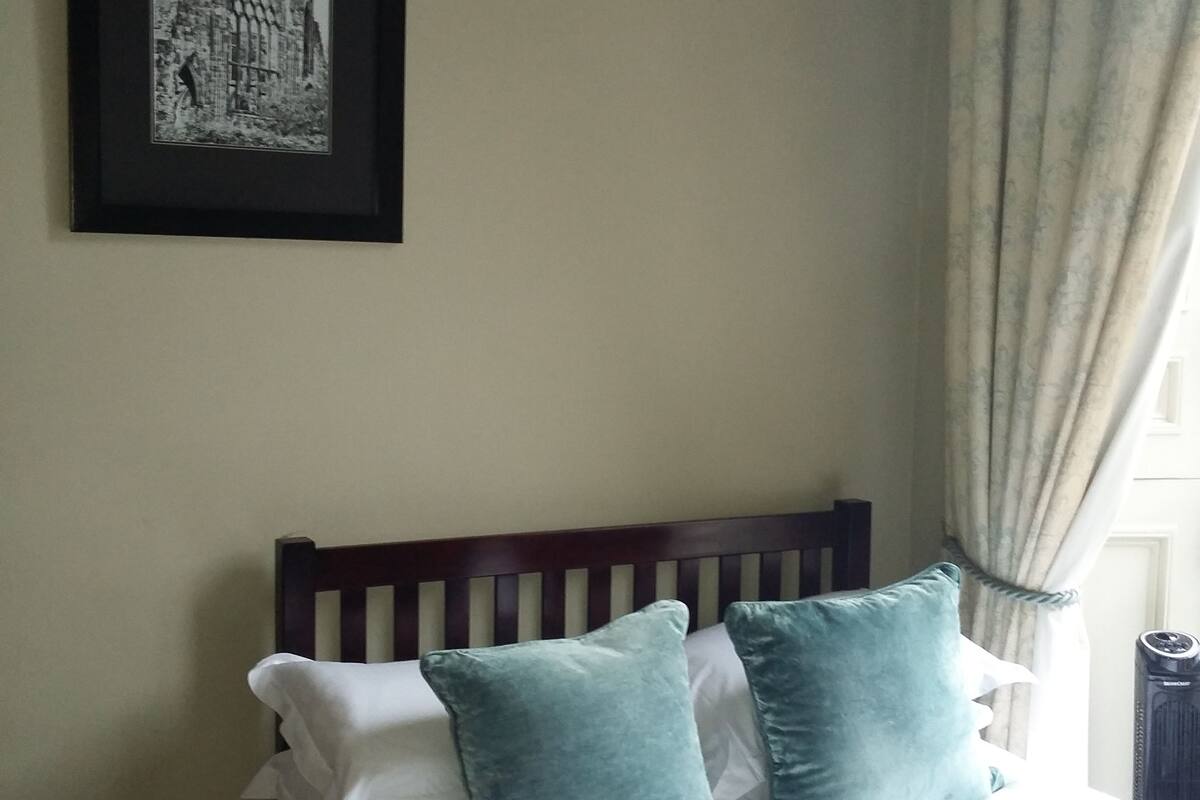 A bedroom with a bed, pillows, a framed picture on the wall, and a window with curtains.