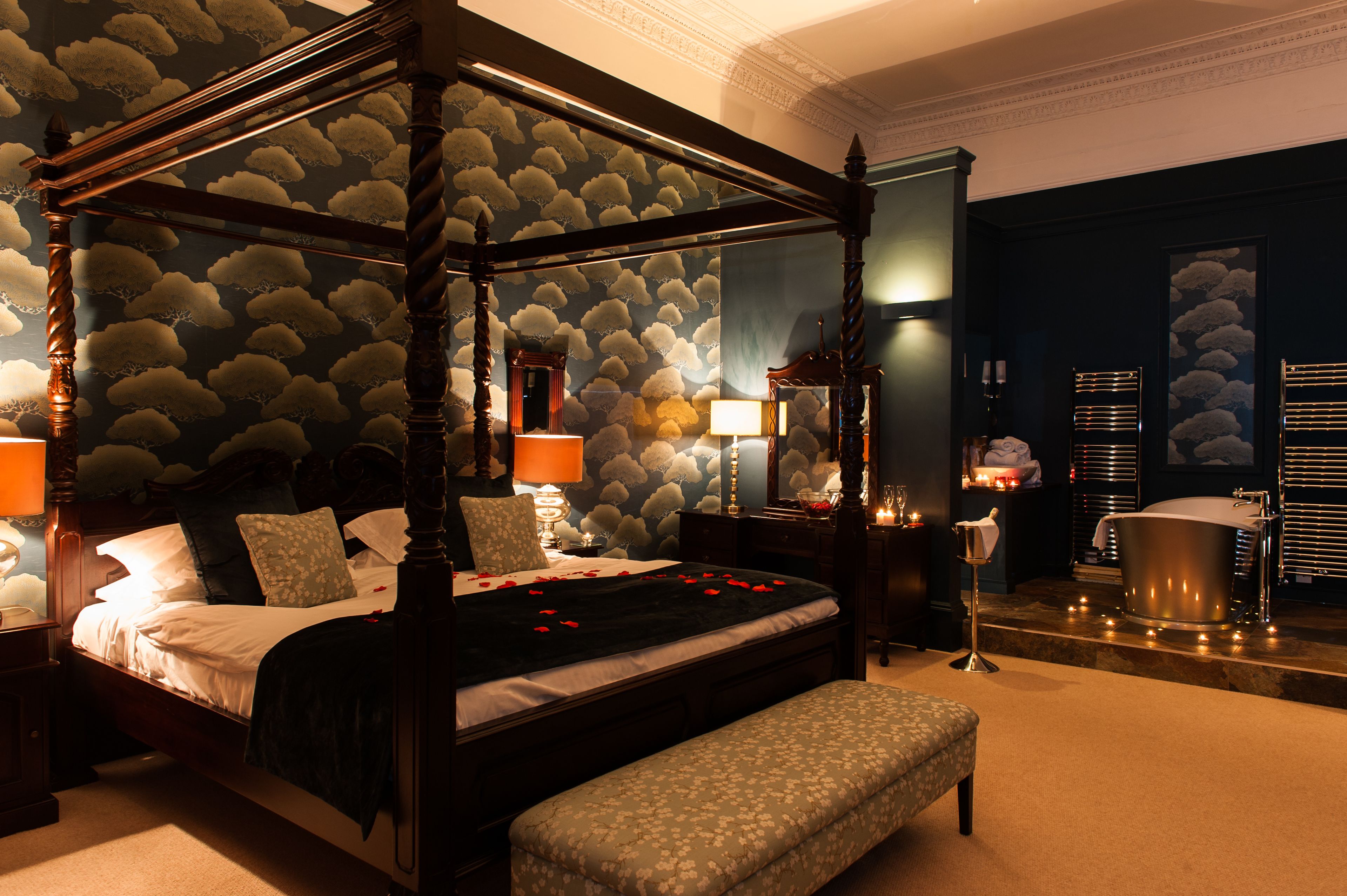 A four-poster bed with rose petals, a bench, a bathtub, and a mirror.