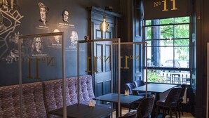 Interior de restaurant amb una paret fosca que mostra figures històriques i una citació, un terra de fusta i una vista al carrer a través d'una finestra gran.