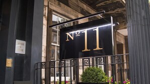 Un senyal de metall negre amb la inscripció “No 11” en lletres daurades, una barana de metall negre i una jardiniere amb flors.
