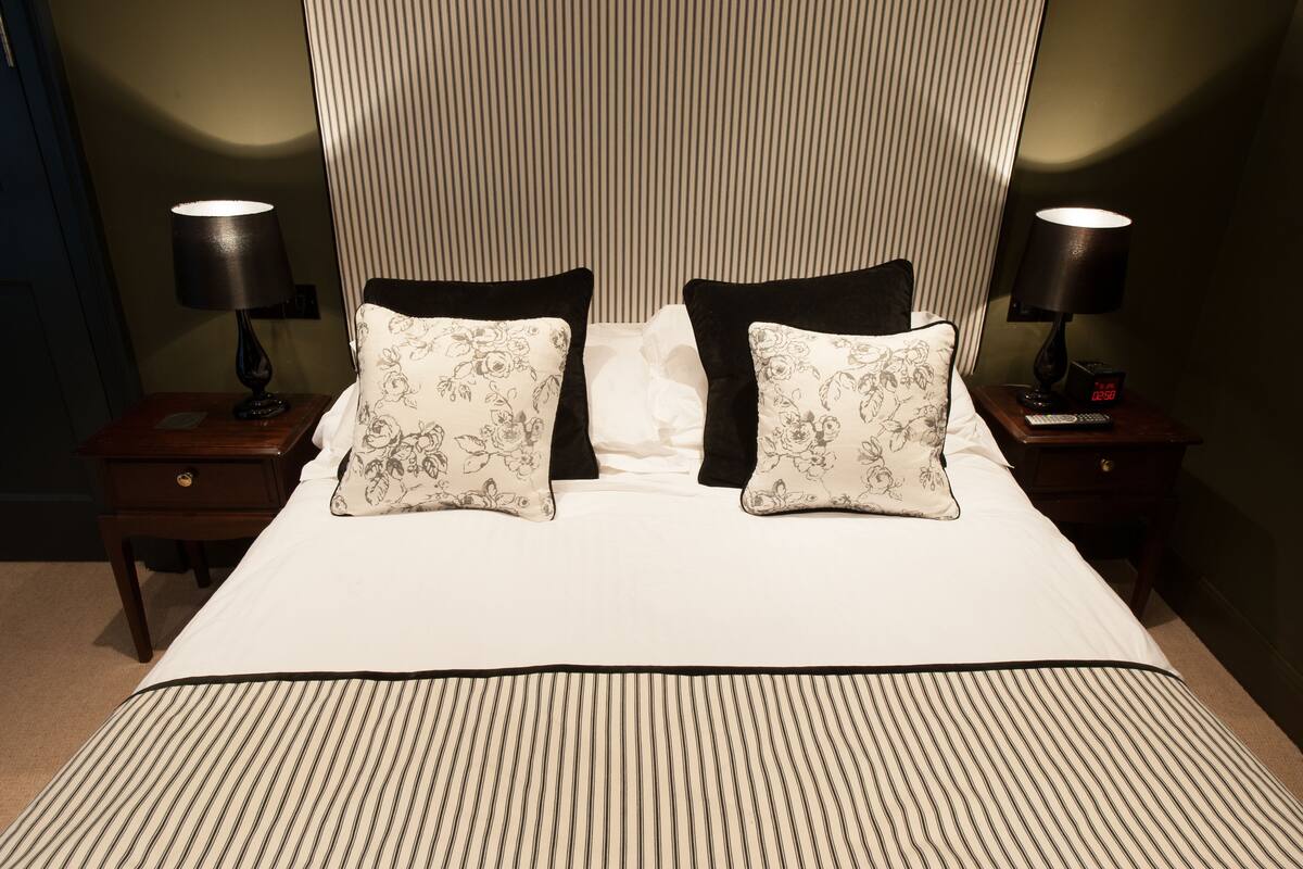 A neatly made bed with floral pillows, two bedside tables with lamps, and a digital clock.