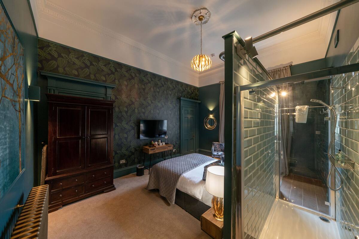 A bedroom with a large wardrobe, a bed, a television, and a glass-enclosed shower.