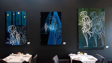 Three artworks on a wall in a dining area with tables set for dining.