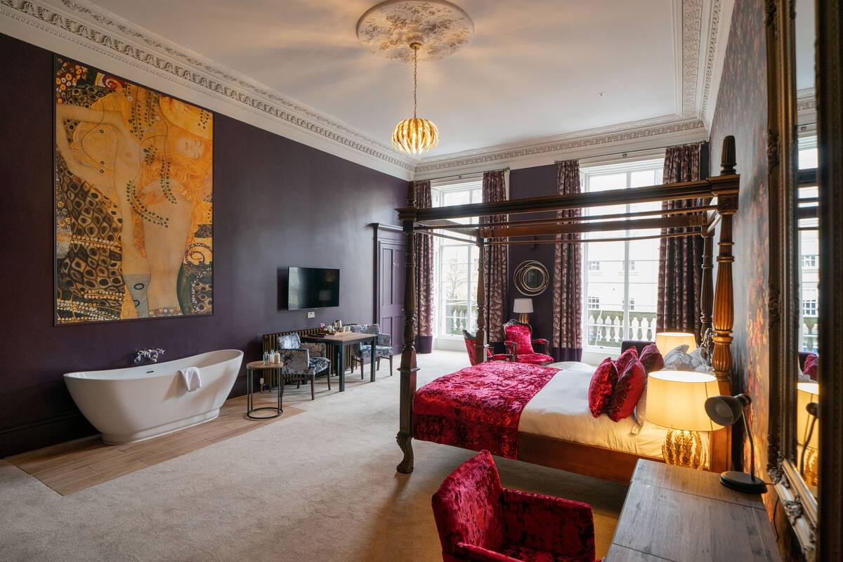 A luxurious bedroom with a large bed, a clawfoot bathtub, and a dining area.