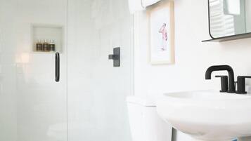 Une salle de bain moderne avec des toilettes blanches, une douche à parois de verre et un lavabo blanc doté d’un robinet noir.