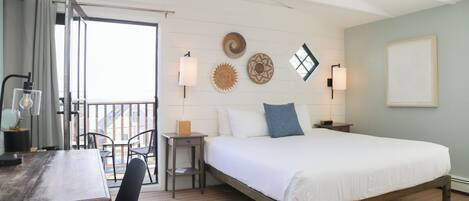 A bedroom with a bed, a desk, and a chair. There is a window with curtains, a ceiling fan, and wall-mounted lamps.
