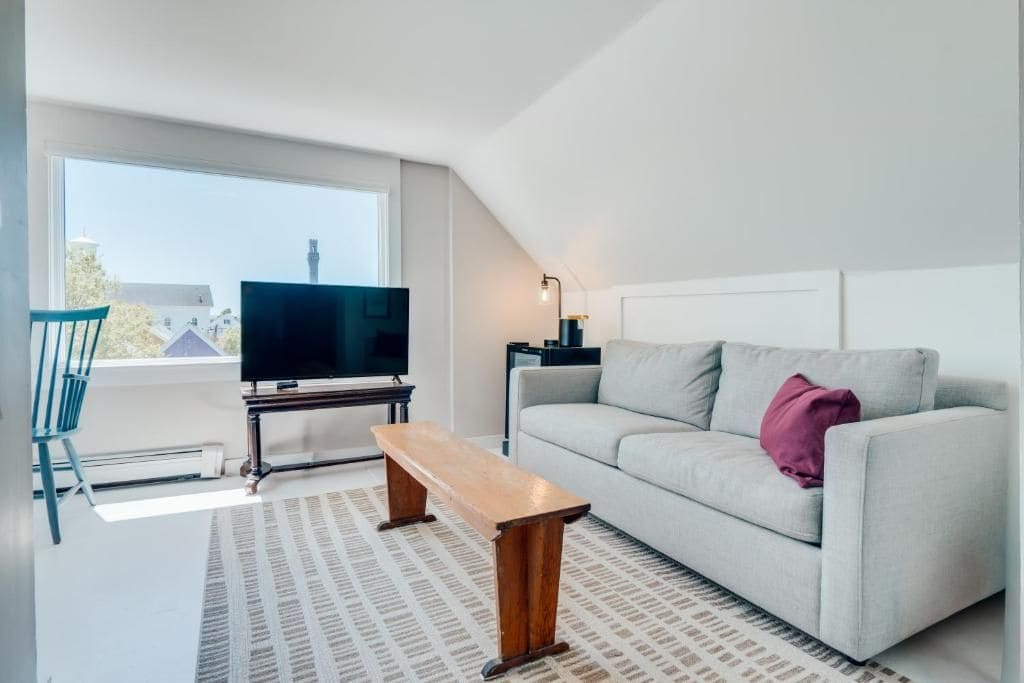 A modern living room with a television, sofa, bench, and a patterned rug.