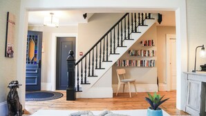 A staircase with black balusters, a bookshelf, a chair, and a potted plant in a living room with wooden flooring. - Waterford Inn Provincetown (Provincetown)