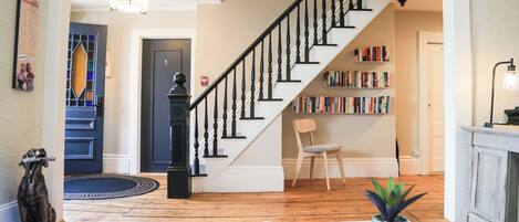 A staircase with black balusters, a bookshelf, a chair, and a potted plant in a living room with wooden flooring.