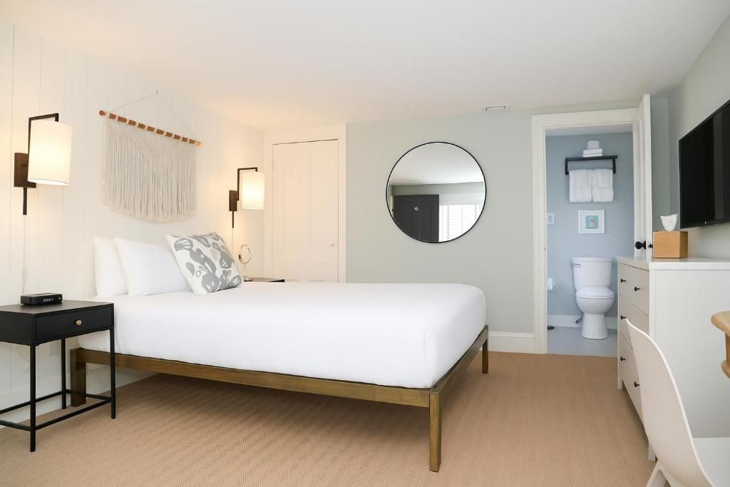Un dormitorio con cama, mesita de noche, lámpara, espejo en la pared y vistas al baño.
