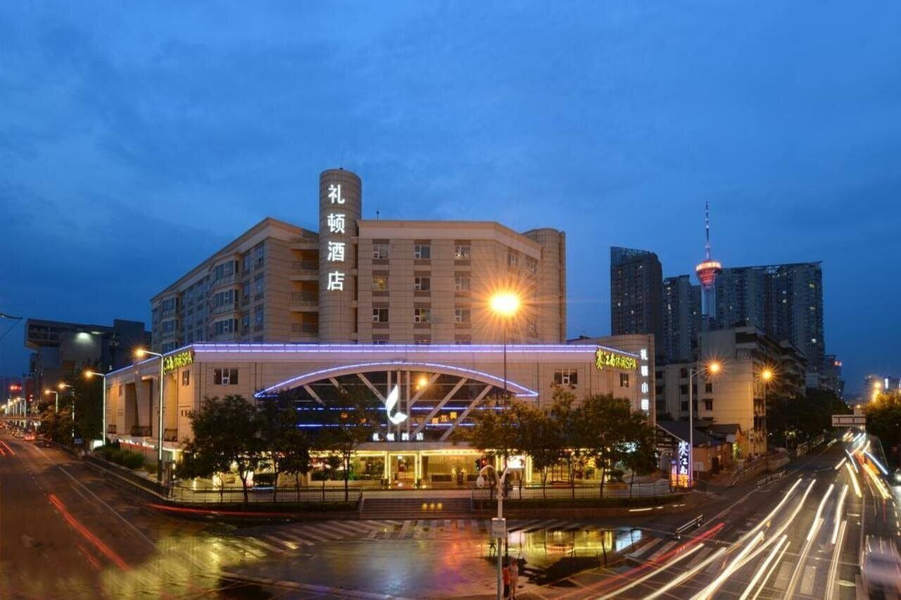 Un hotel con una imponente torre de reloj, una fachada moderna y vistas del horizonte urbano al fondo.