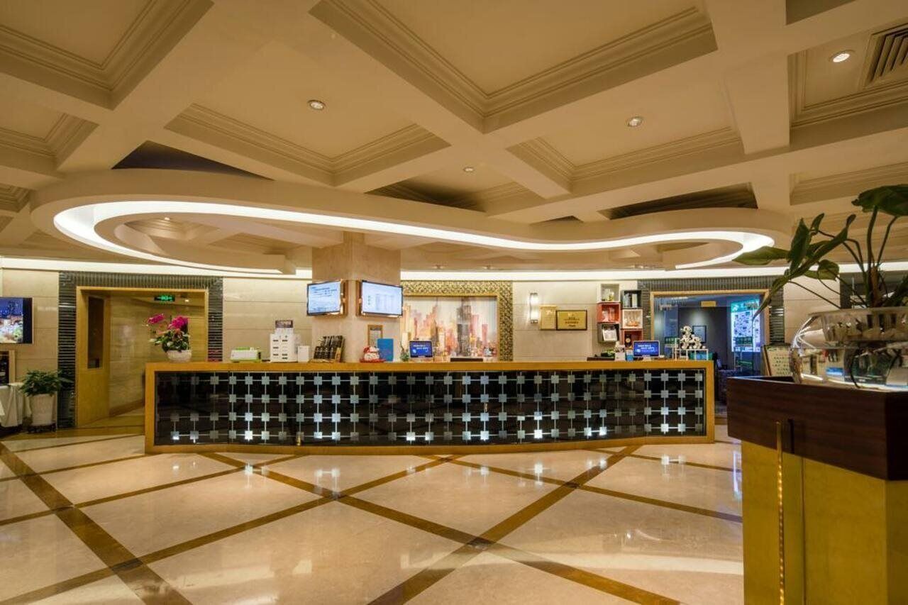 Zona de recepción de hotel con diseño moderno, que incluye un mostrador de recepción, pantallas digitales y suelo de baldosas.