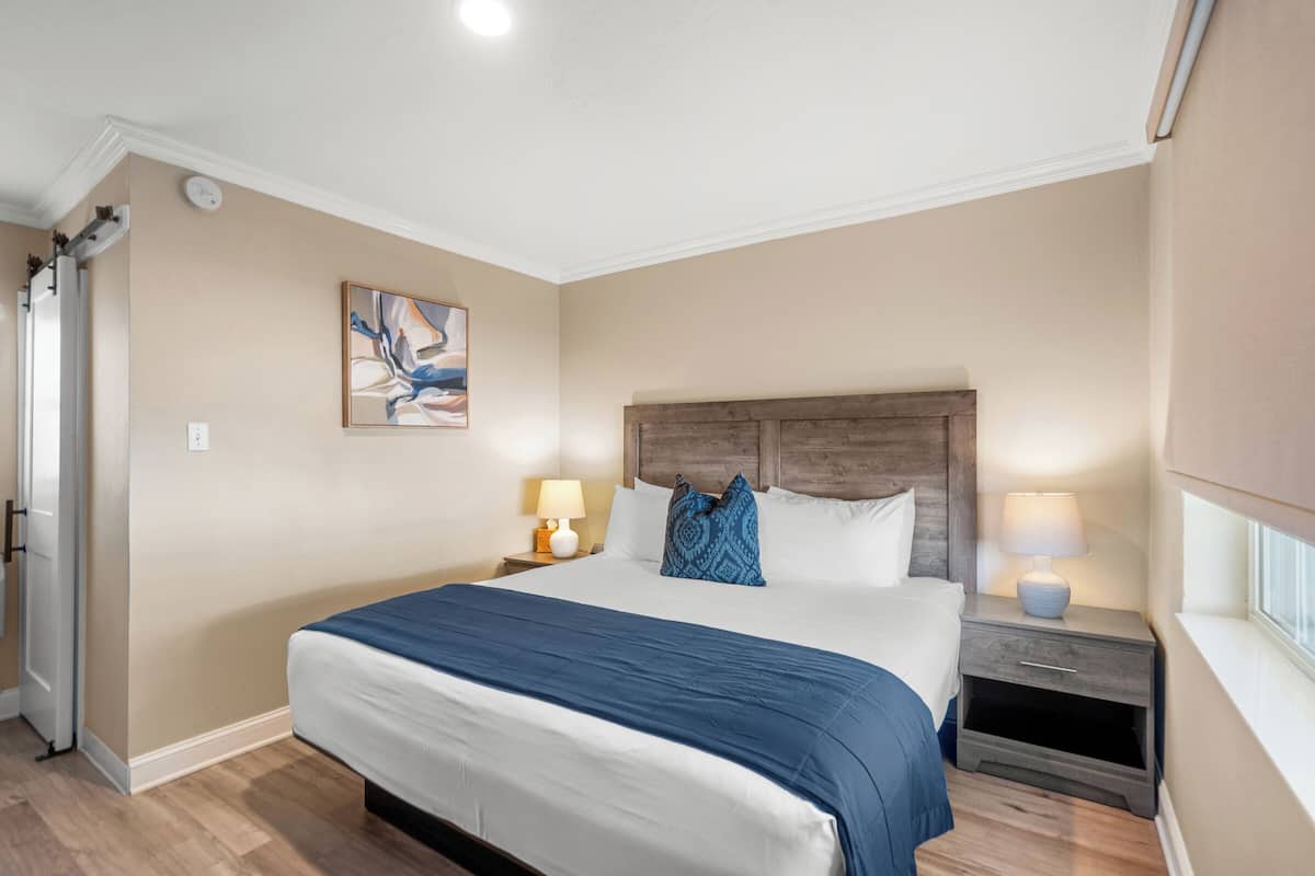 Un dormitorio con una cama grande, cabecera de madera, una mesita de noche con lámpara y una ventana.