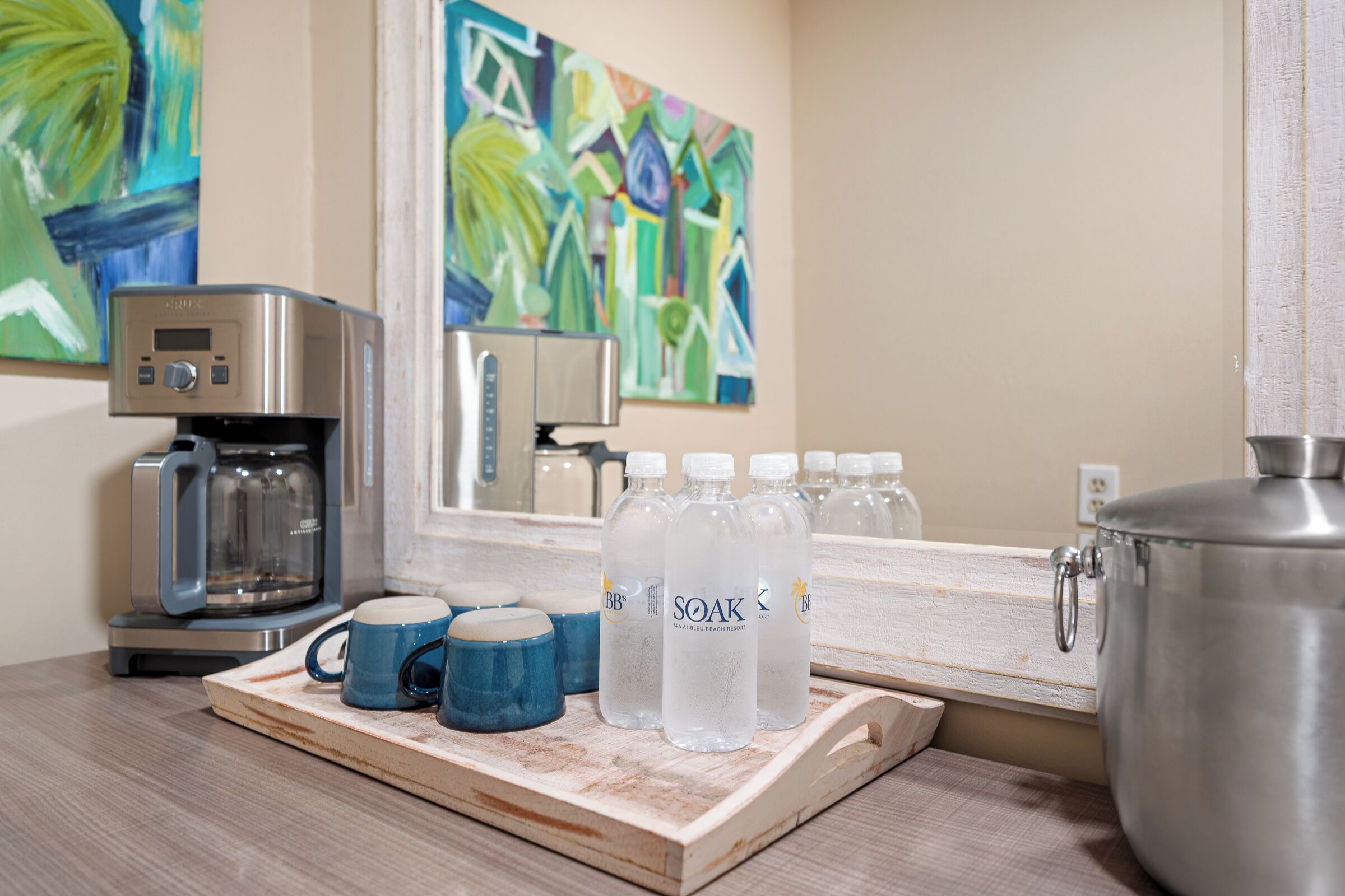 A kitchen area with a coffee maker, a tray with mugs and water bottles, and a large pot.