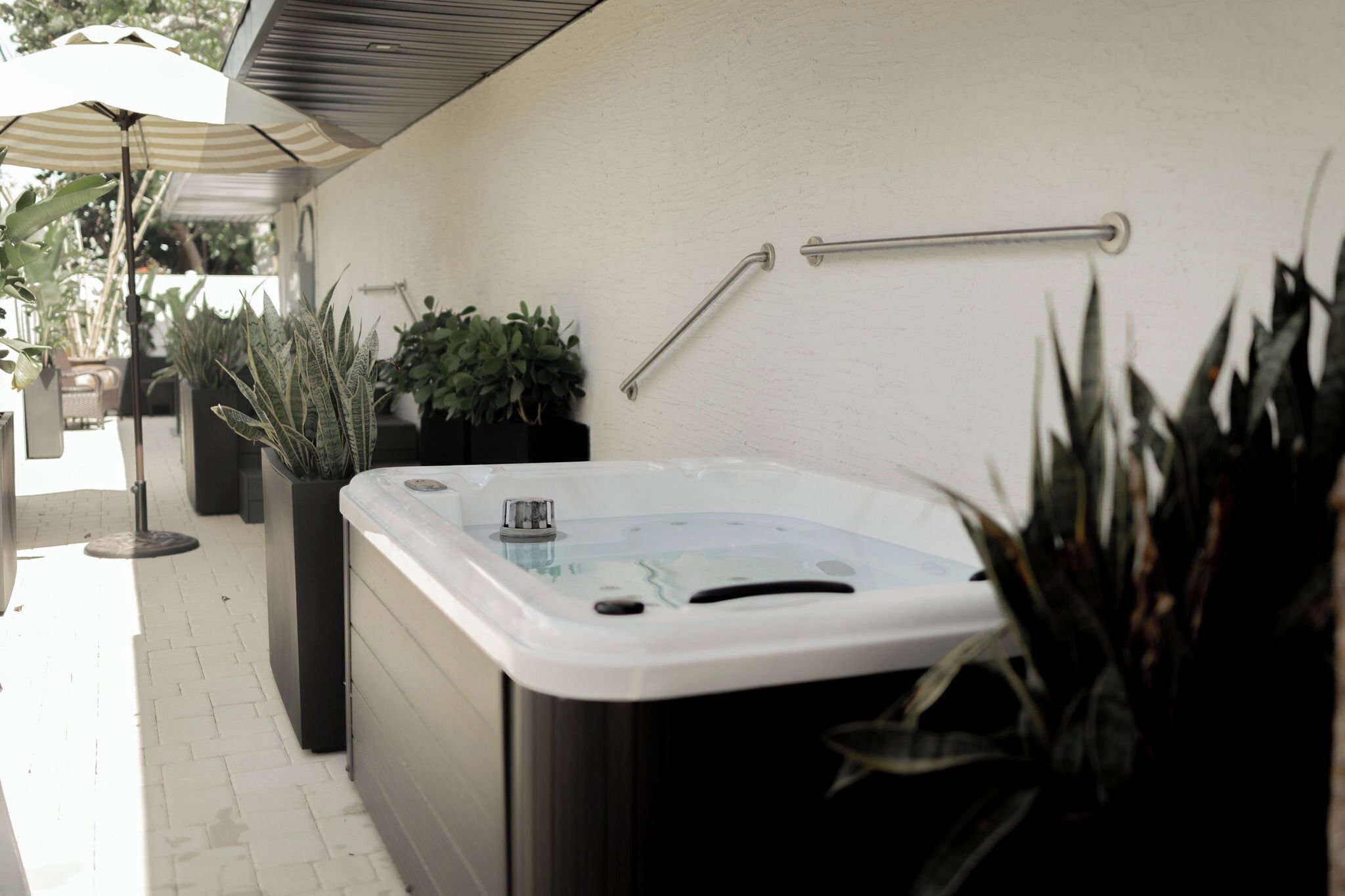 A spa area with a hot tub, potted plants, and a handrail on the wall.