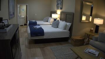 Habitación de hotel con dos camas, un escritorio, una silla, una mesita, una lámpara y un espejo.