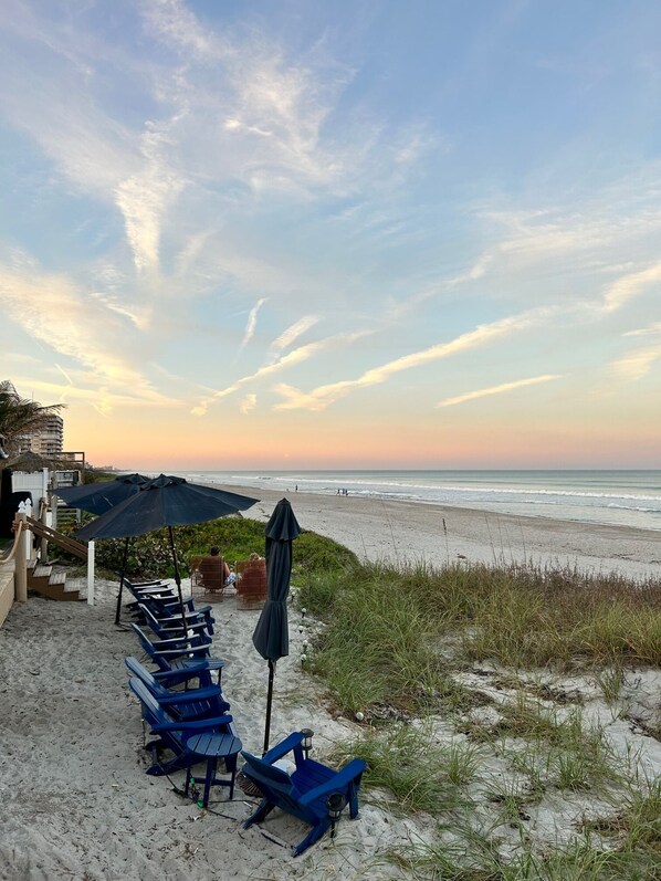 A beachside seating area with lounge chairs and umbrellas, overlooking the ocean.