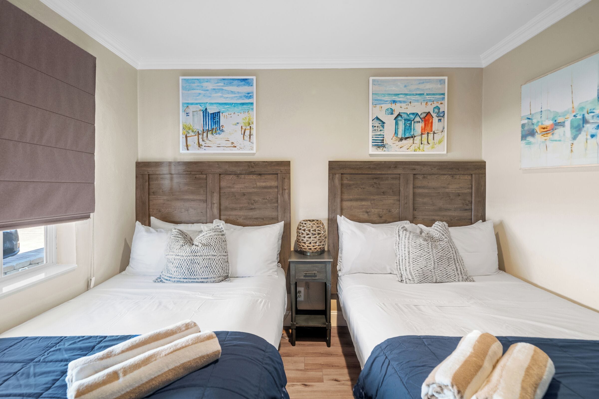 Una habitación de hotel con dos camas, una mesita de noche pequeña y obras de arte en las paredes.