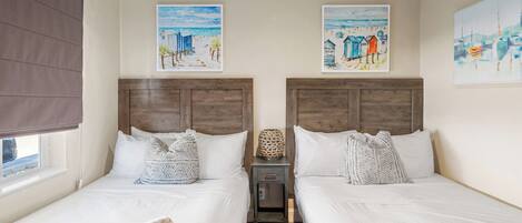 Una habitación de hotel con dos camas, una mesita de noche pequeña y obras de arte en las paredes.