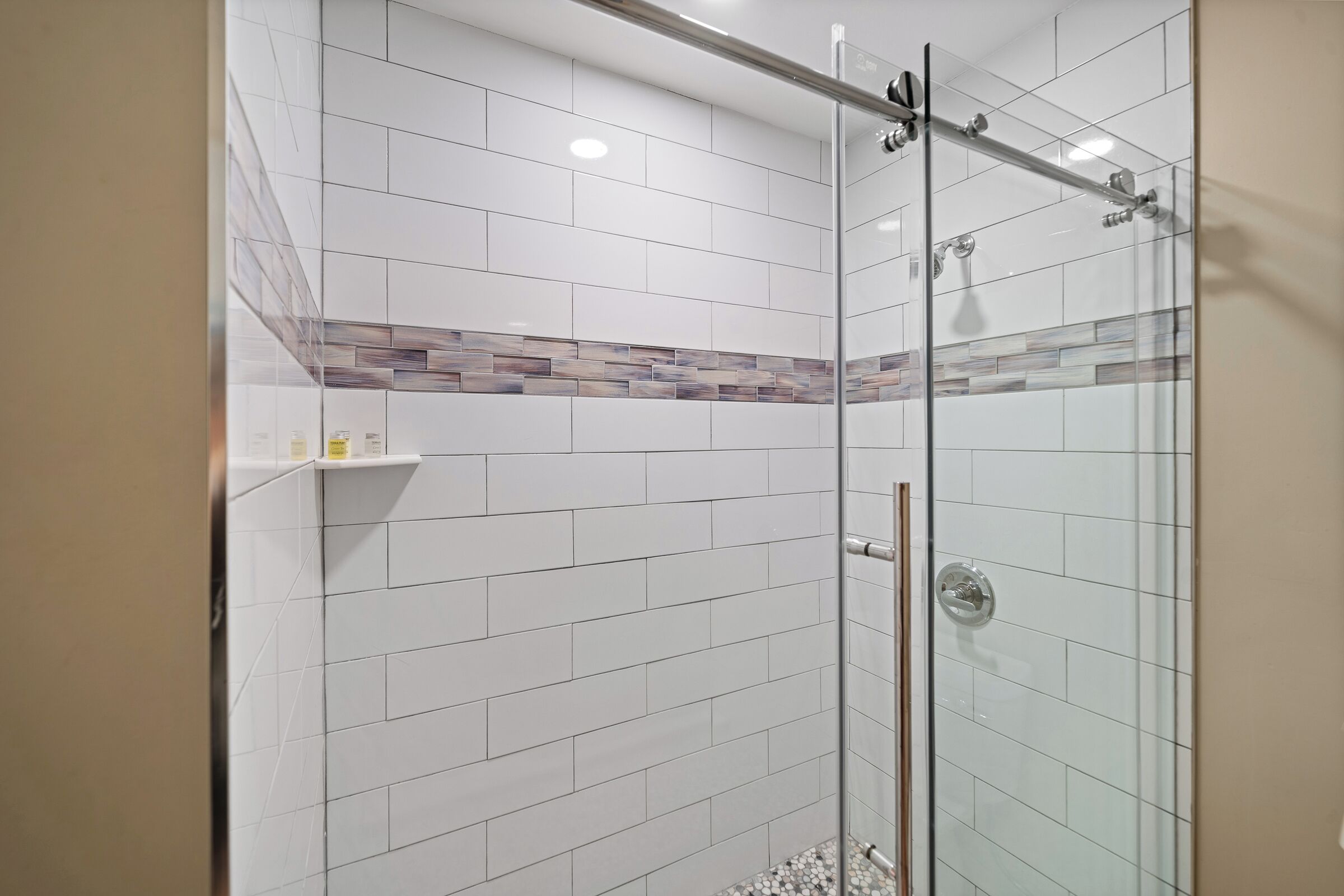 Une douche fermée par des parois de verre, avec des carreaux blancs et une bordure décorative.