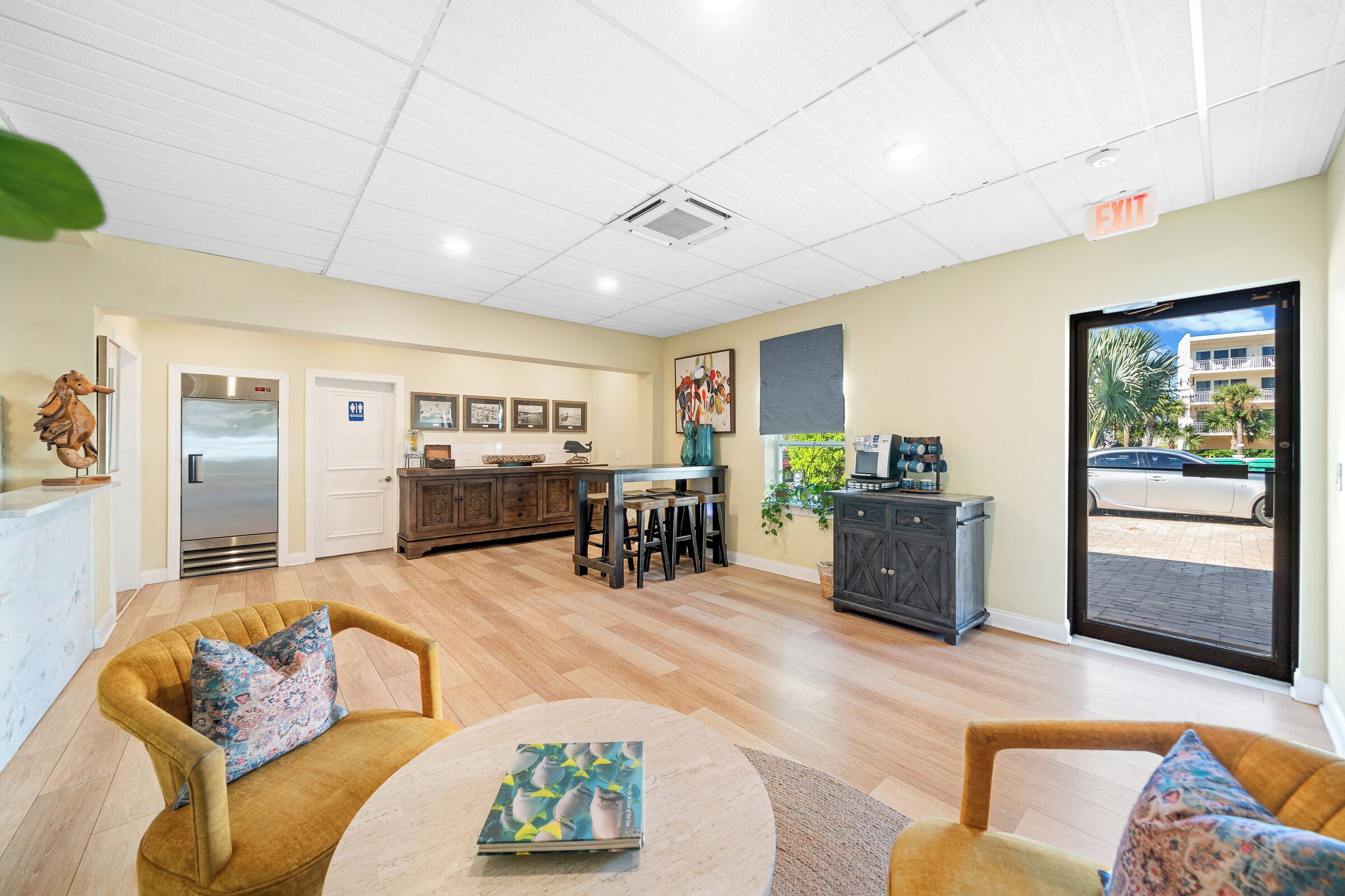 A spacious lobby with a wooden floor, a reception desk, a refrigerator, and a dining area with chairs and tables.