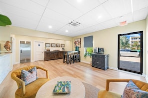 A spacious lobby with a wooden floor, a reception desk, a refrigerator, and a dining area with chairs and tables. - Bleu Beach Resort (Indialantic)