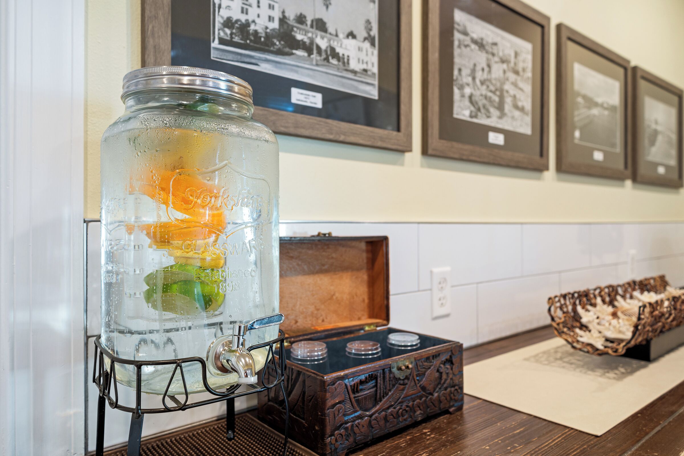 A large glass jar with a pump dispenser filled with fruit slices, placed on a metal stand.