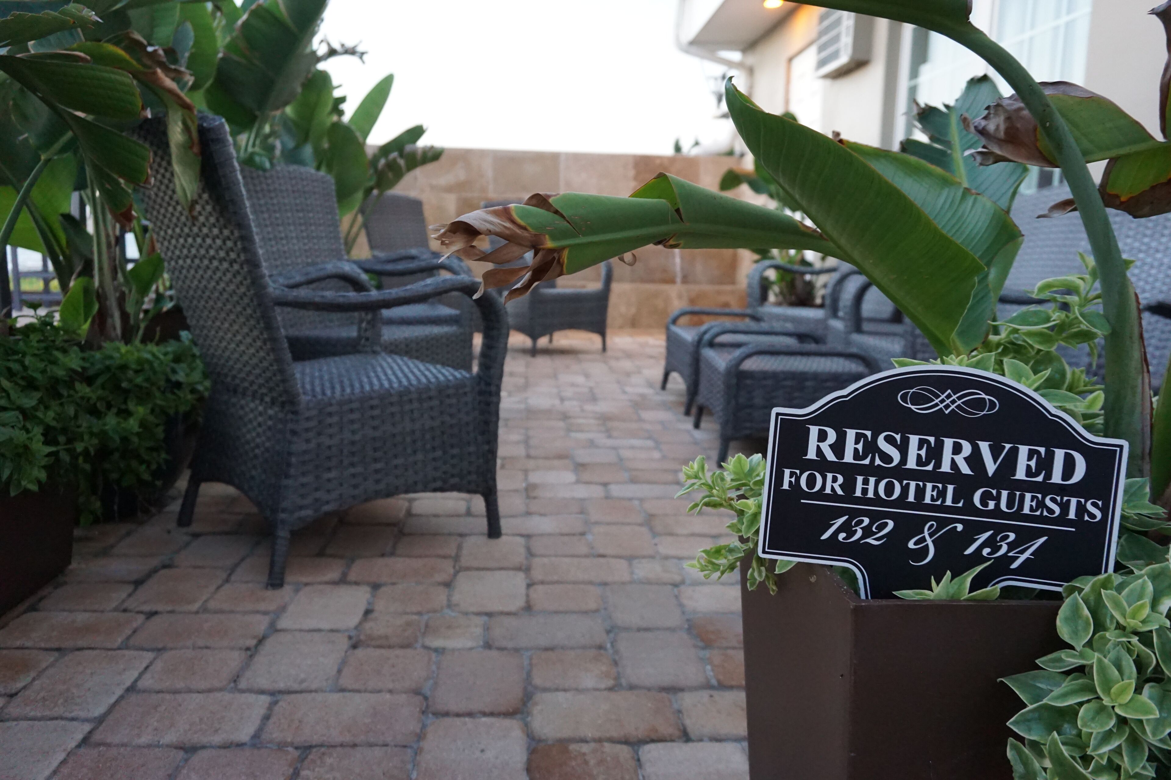 Un espace patio aménagé avec des meubles en osier et un panneau indiquant les places de stationnement réservées aux clients de l’hôtel.