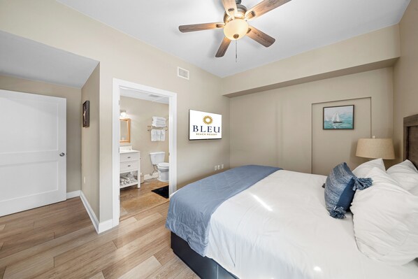 A bedroom with a bed, a ceiling fan, a bathroom visible through an open door, and a sign reading "BLEU BEACH RESORT".
