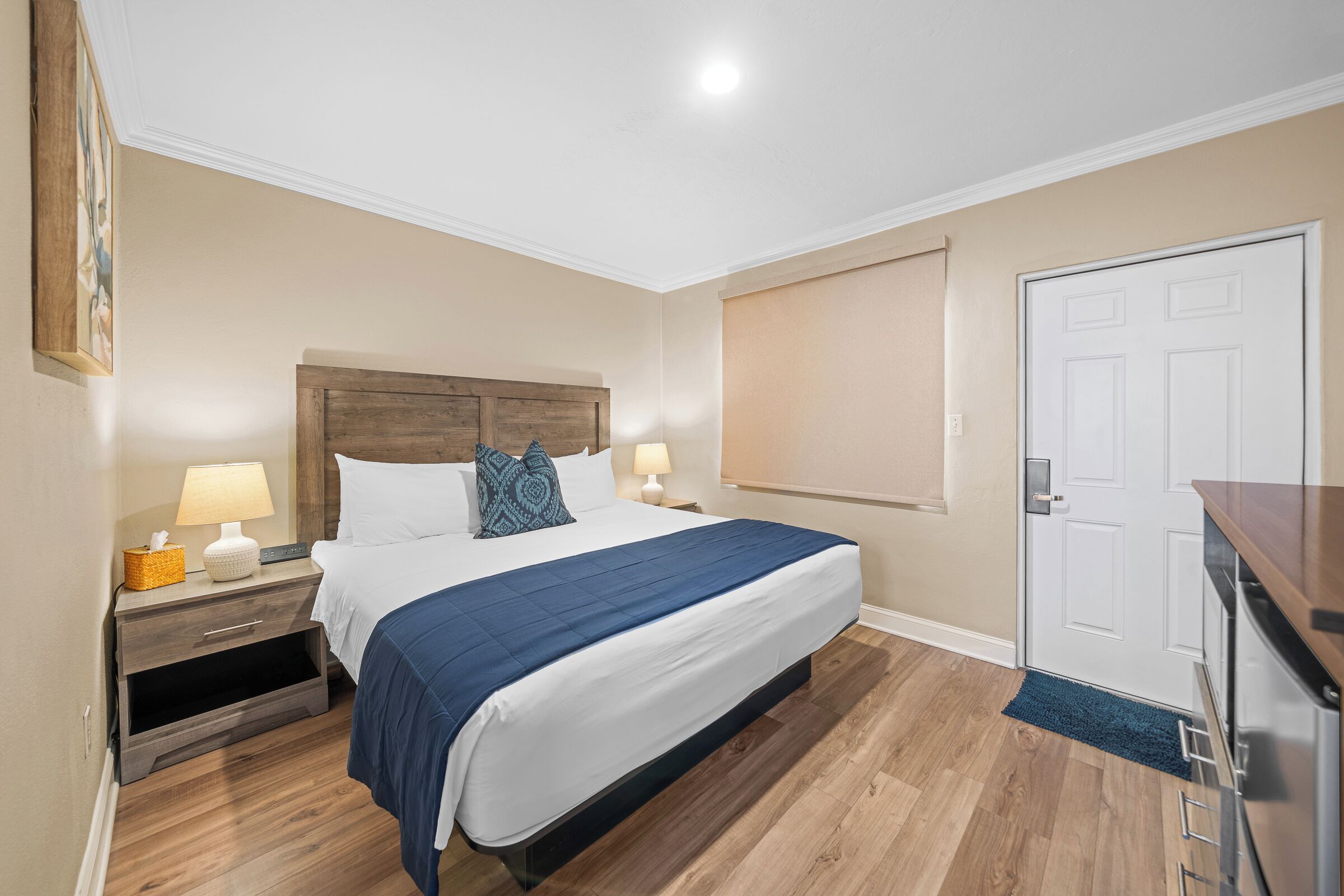 A bedroom with a bed, nightstands, a wooden headboard, a white door, and a wooden floor.