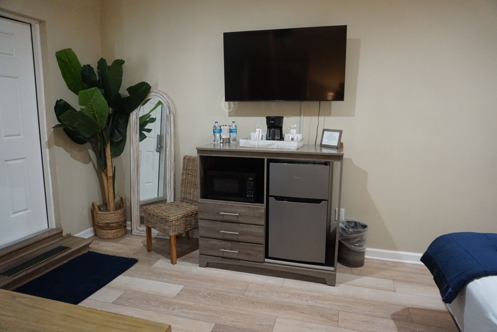 Une chambre d’hôtel compacte, dotée d’une kitchenette, d’un téléviseur à écran plat, d’une plante en pot et d’un fauteuil en osier.