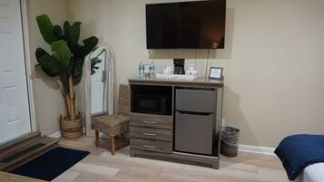 Une chambre d’hôtel compacte, dotée d’une kitchenette, d’un téléviseur à écran plat, d’une plante en pot et d’un fauteuil en osier.