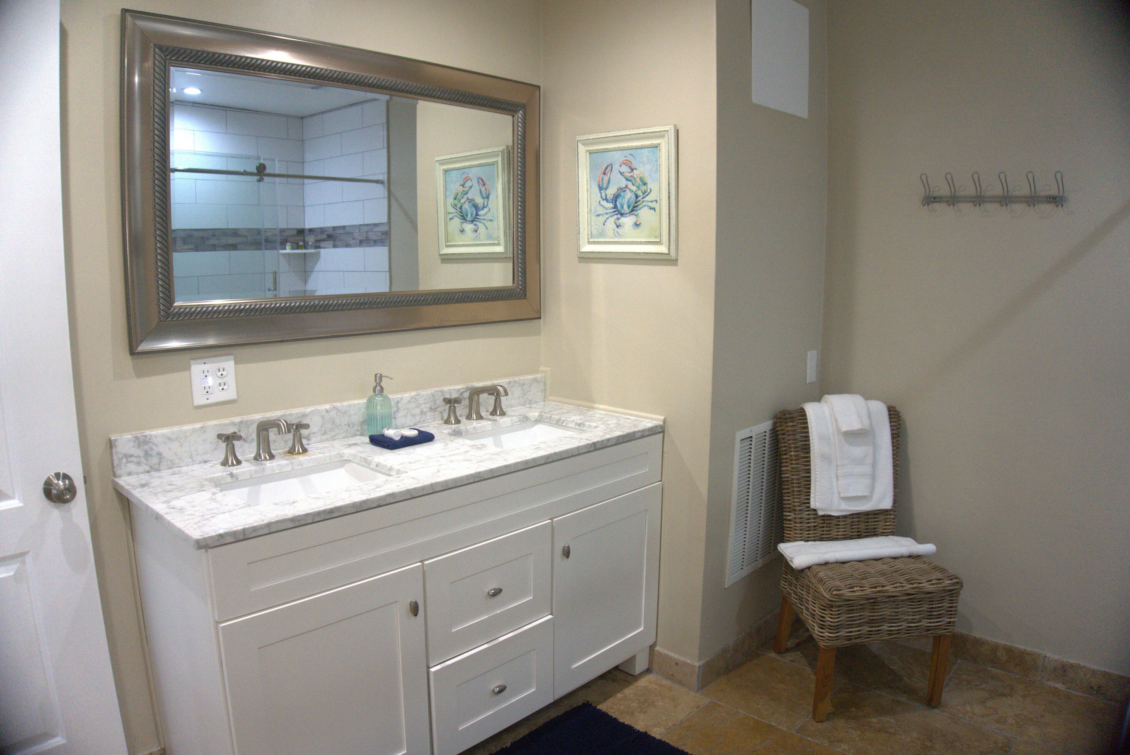 A bathroom with a double sink vanity, a large mirror, and a wicker chair with a towel.