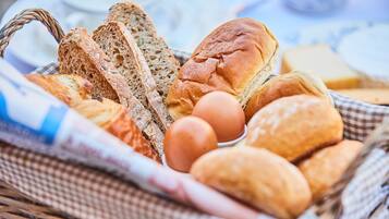 A basket containing various types of bread, including whole grain and baguette, along with a few eggs.