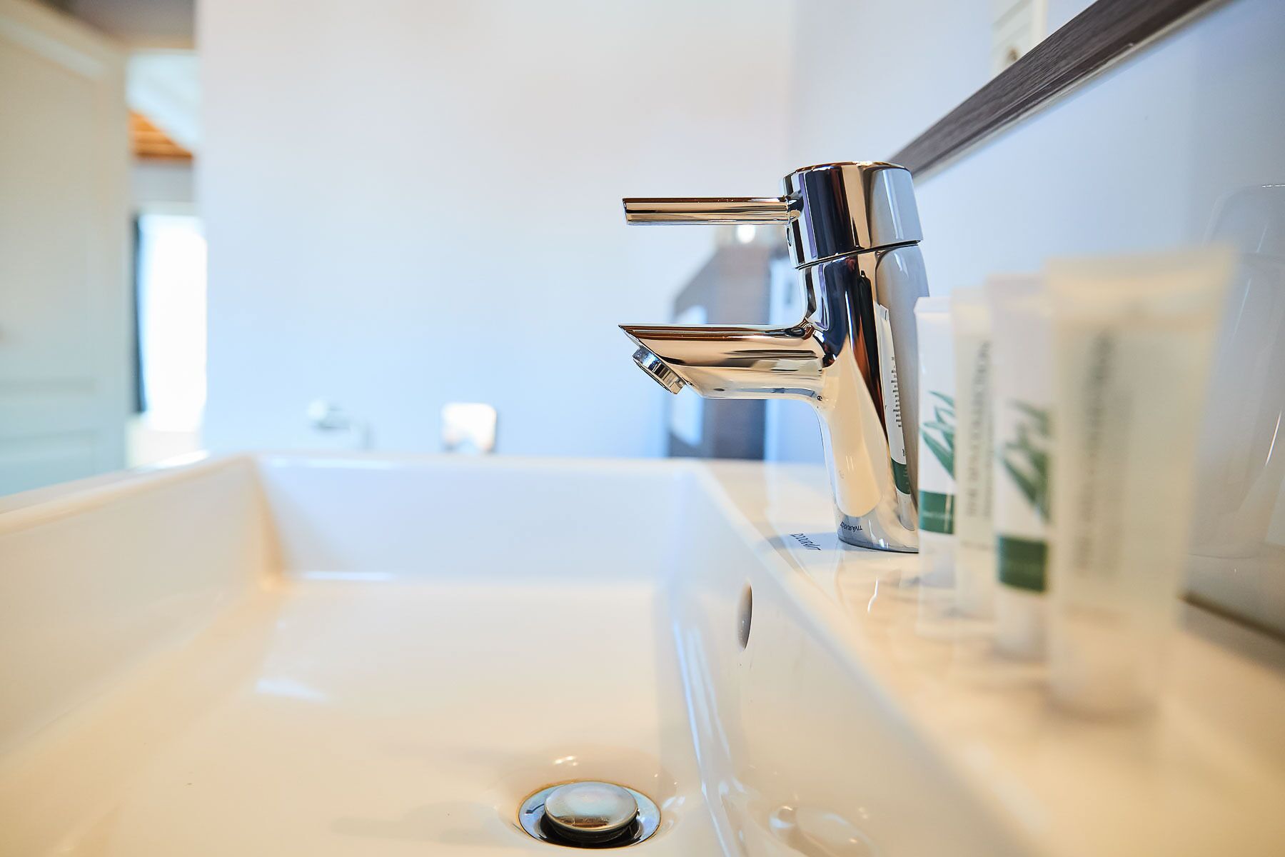 A modern bathroom sink with a chrome faucet, a mirror above it, and toiletries on the countertop.