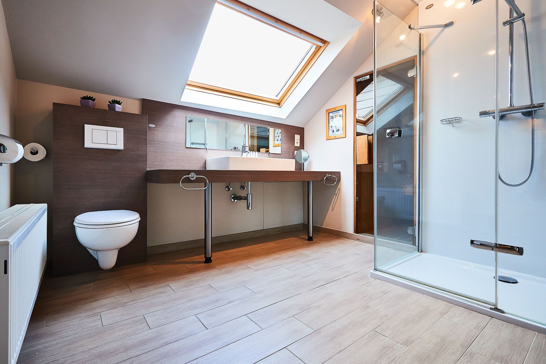 Une salle de bain moderne dotée d’un puits de lumière, d’une cabine de douche en verre et d’un plancher en bois.