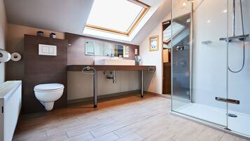 Une salle de bain moderne dotée d’un puits de lumière, d’une cabine de douche en verre et d’un plancher en bois.