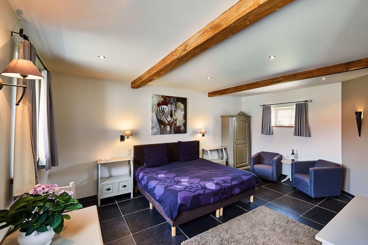 Um quarto com cama, mesas de cabeceira, escrivaninha, cadeira, guarda-roupa e um quadro na parede.