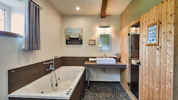 Een moderne badkamer met een groot bad, een wastafel en een spiegel. Aan de ene kant is houten wandbekleding en er ligt een betegelde vloer.