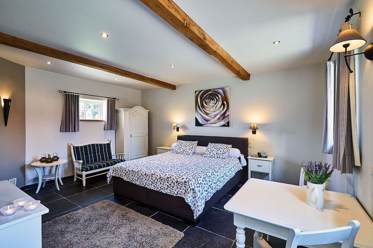 Um quarto com cama, mesas de cabeceira, escrivaninha, cadeira, guarda-roupa e um quadro na parede.