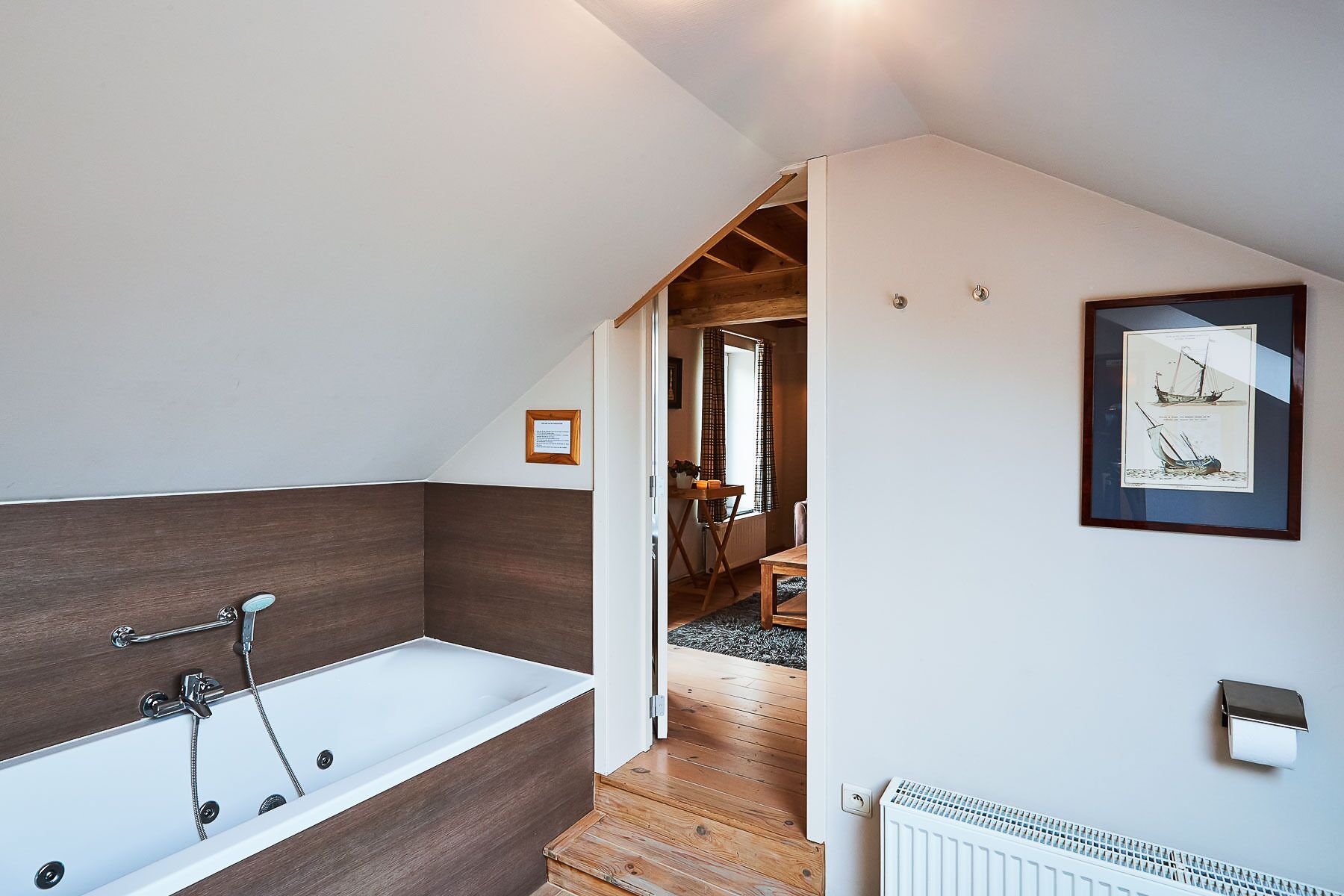 A modern bathroom with a bathtub, wooden paneling, and a framed nautical illustration on the wall.
