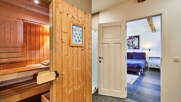 Un interior de madera con una sauna, una puerta blanca que da a un dormitorio con una cama y un cuadro de cebra.