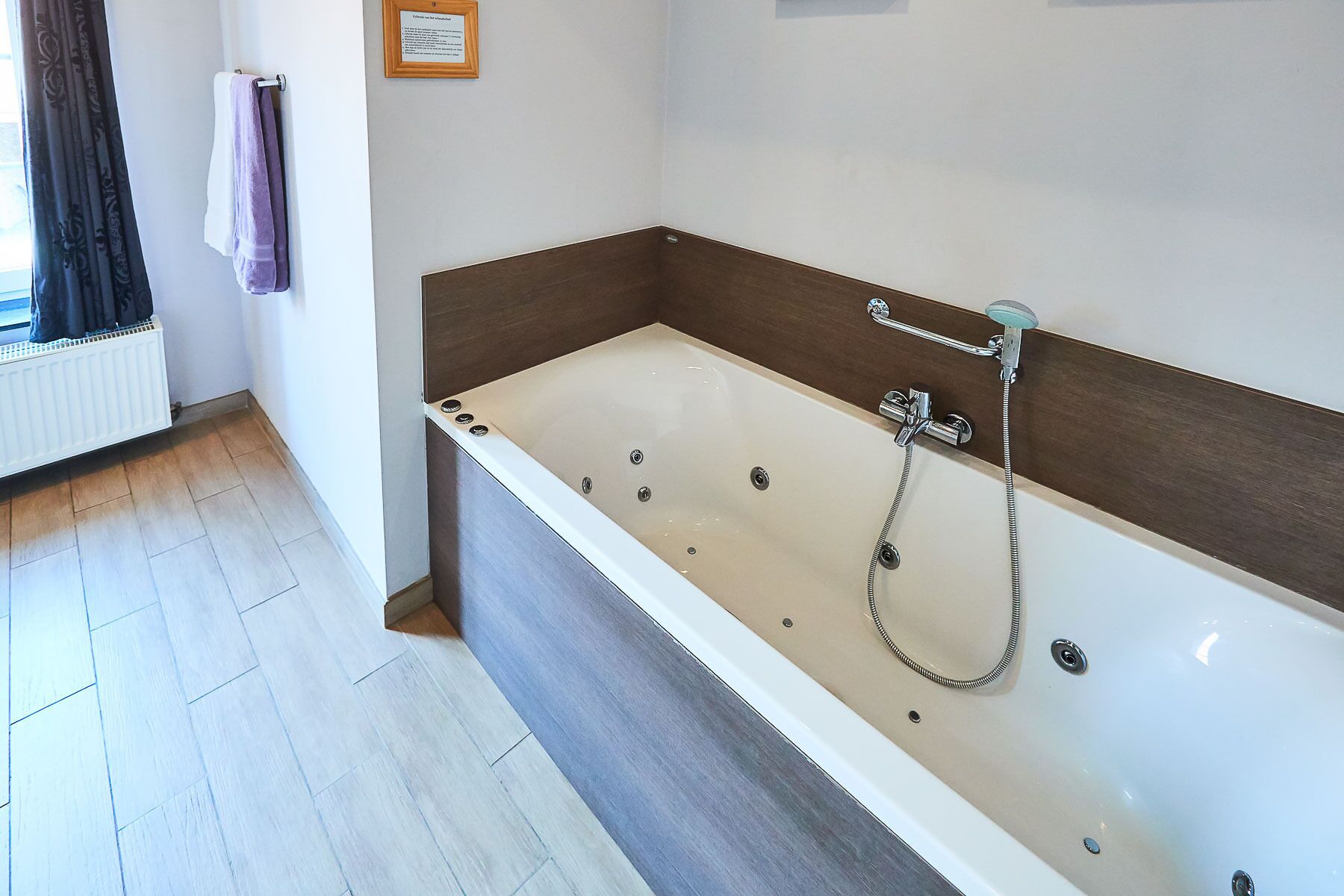 A modern bathroom with a large bathtub, a showerhead, and a towel rack.