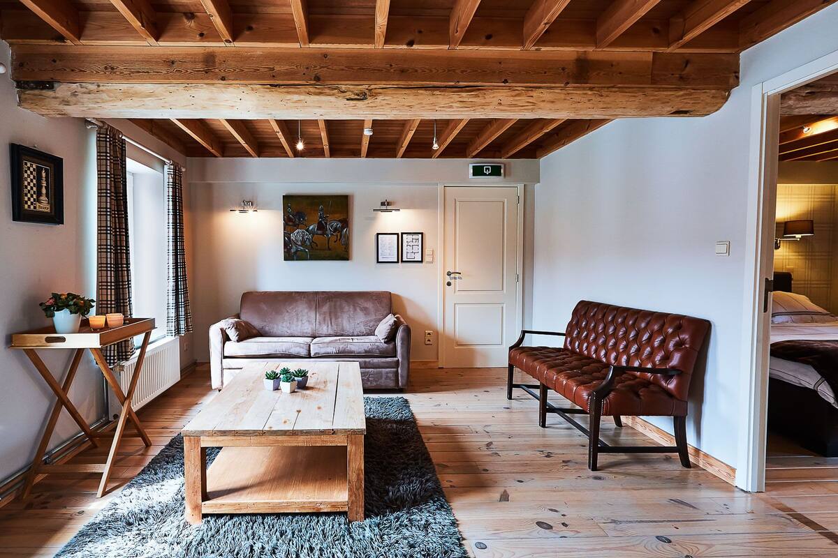 Uma sala de estar acolhedora com teto de madeira, um sofá de couro marrom, uma mesa de centro de madeira e um tapete.