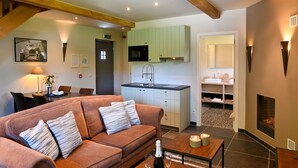 Een gezellige woonkamer met een bruine bank, een eettafel en een keuken met lichtgroene kastjes en een zwarte magnetron.