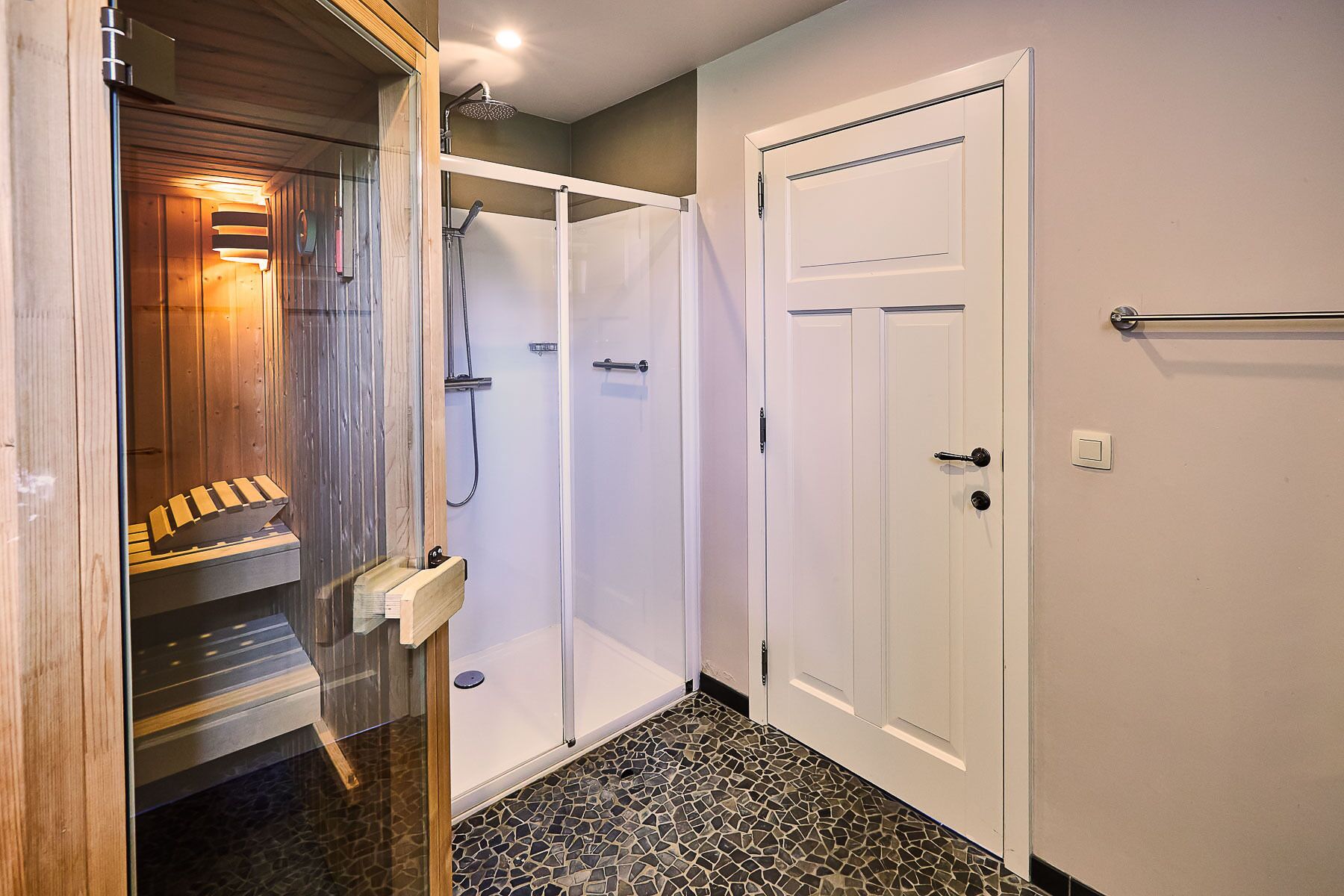 Een hal met een sauna, een douche en een deur met een handdoekhouder.