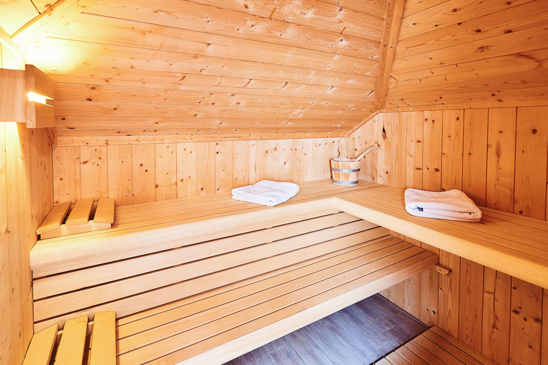 A wooden sauna with benches and a bench seat, a bucket, and a towel.